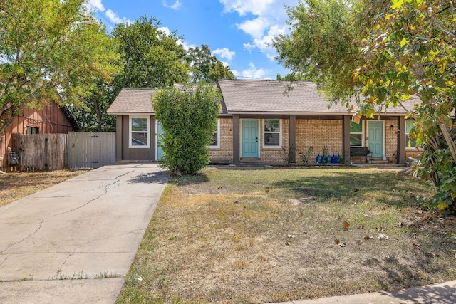 single story home featuring a front lawn, driveway, fence, a shingled roof, and brick siding