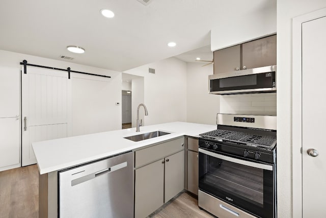 kitchen with visible vents, a peninsula, a sink, stainless steel appliances, and light countertops