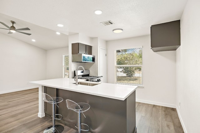 kitchen with visible vents, light wood finished floors, light countertops, appliances with stainless steel finishes, and a kitchen bar