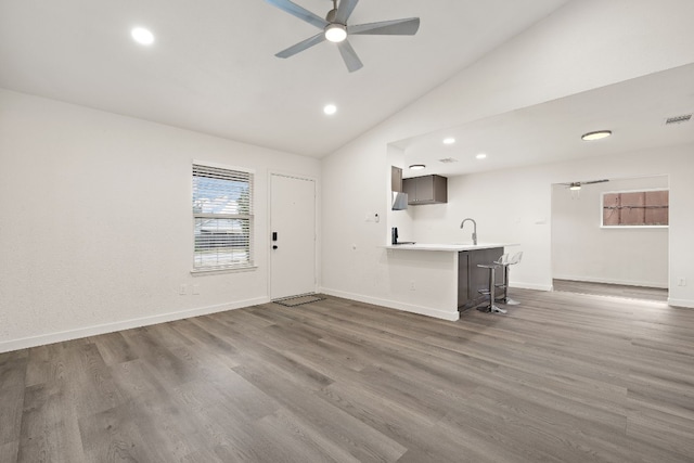 unfurnished living room with a ceiling fan, baseboards, dark wood-style flooring, a sink, and vaulted ceiling