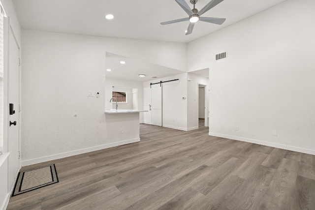 unfurnished living room with visible vents, wood finished floors, a barn door, lofted ceiling, and ceiling fan