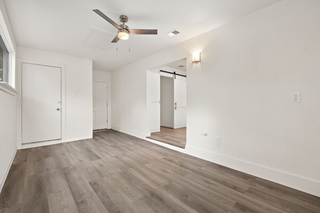 unfurnished bedroom featuring visible vents, baseboards, wood finished floors, and a barn door