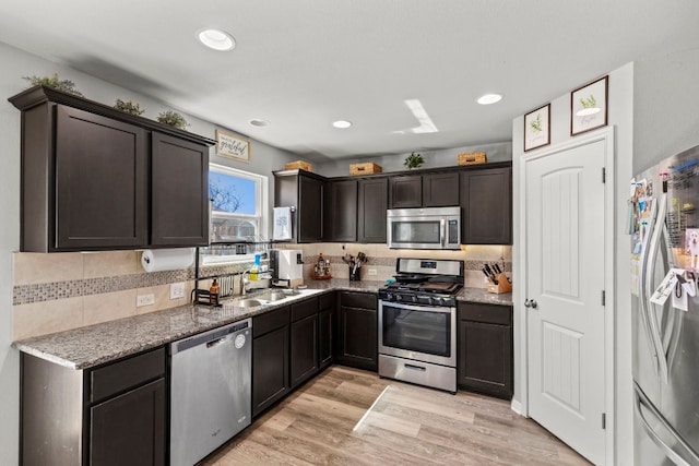 kitchen featuring light stone counters, a sink, dark brown cabinets, light wood-style floors, and appliances with stainless steel finishes