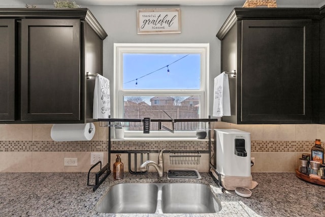 room details featuring a sink, light stone counters, tasteful backsplash, and dark cabinets