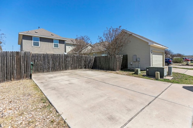 exterior space with central air condition unit, concrete driveway, an attached garage, and fence