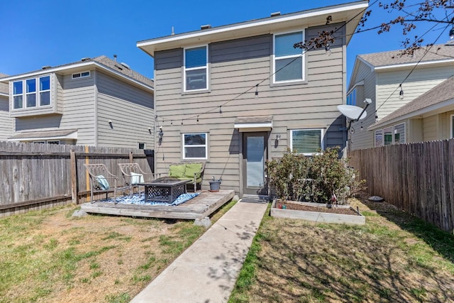 back of property featuring a lawn, a deck, a fenced backyard, a fire pit, and a garden