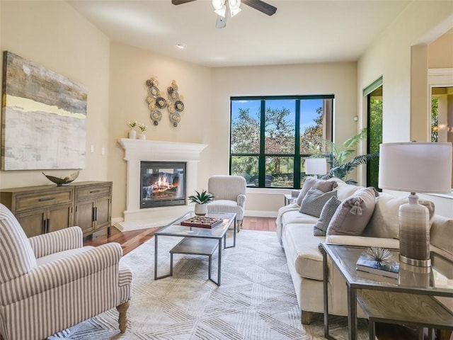 living area with a glass covered fireplace, baseboards, light wood finished floors, and ceiling fan