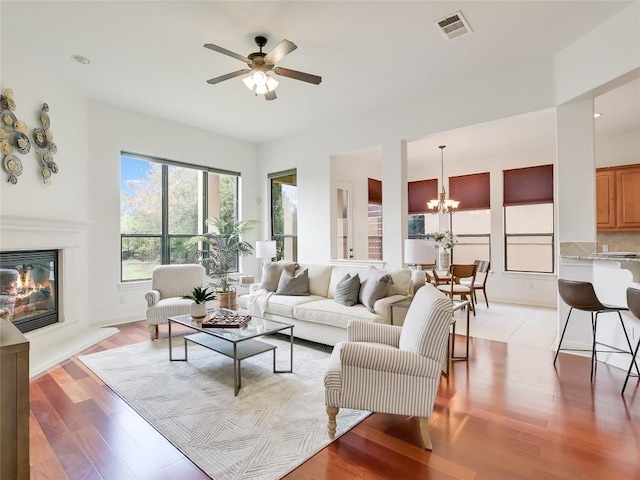 living room with visible vents, ceiling fan with notable chandelier, a glass covered fireplace, and light wood finished floors