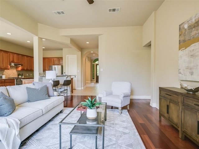 living area featuring visible vents, arched walkways, light wood-style floors, and baseboards