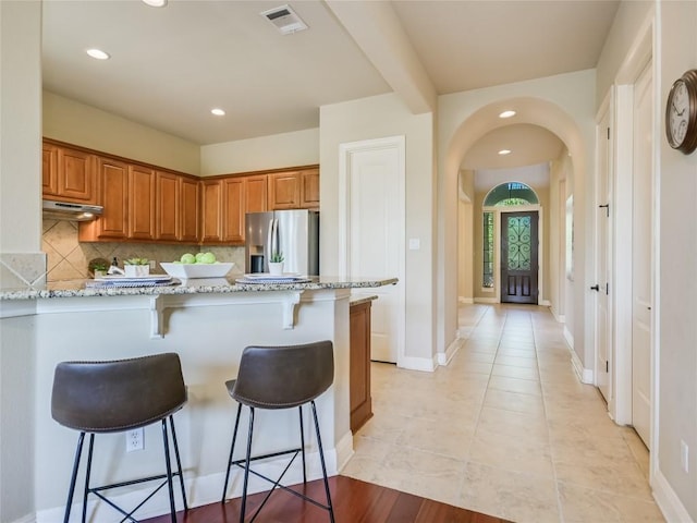 kitchen with brown cabinetry, visible vents, a breakfast bar, stainless steel fridge with ice dispenser, and arched walkways