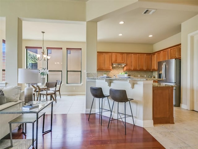 kitchen featuring under cabinet range hood, a kitchen breakfast bar, brown cabinets, and stainless steel refrigerator with ice dispenser