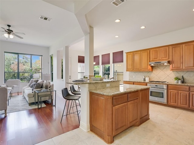 kitchen with oven, visible vents, under cabinet range hood, and open floor plan