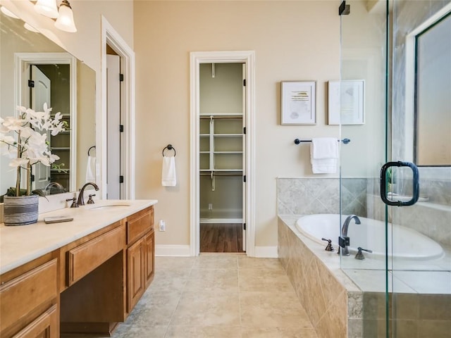 bathroom with a garden tub, vanity, tile patterned flooring, baseboards, and a spacious closet