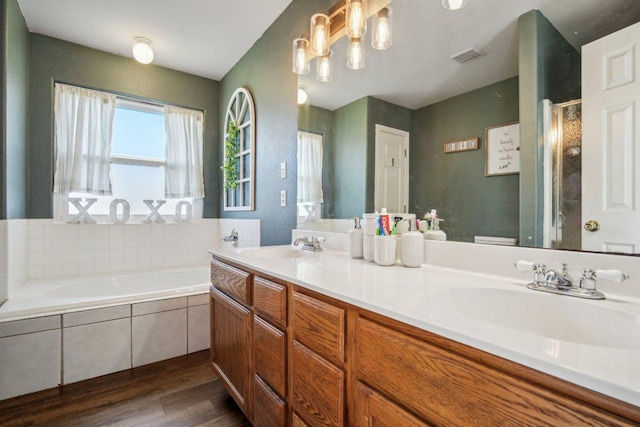 bathroom with visible vents, double vanity, wood finished floors, a bath, and a sink