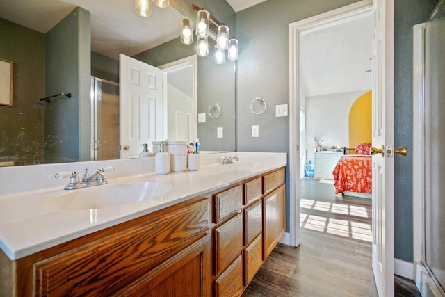 full bathroom featuring wood finished floors, a shower with shower door, double vanity, a sink, and ensuite bathroom