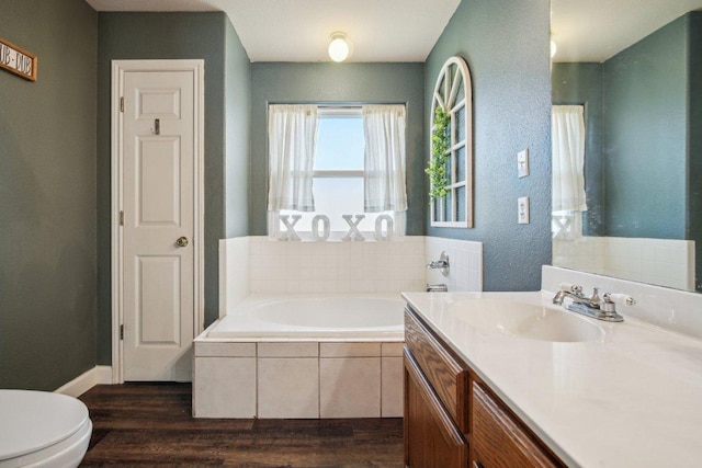 bathroom with toilet, wood finished floors, a garden tub, a textured wall, and vanity