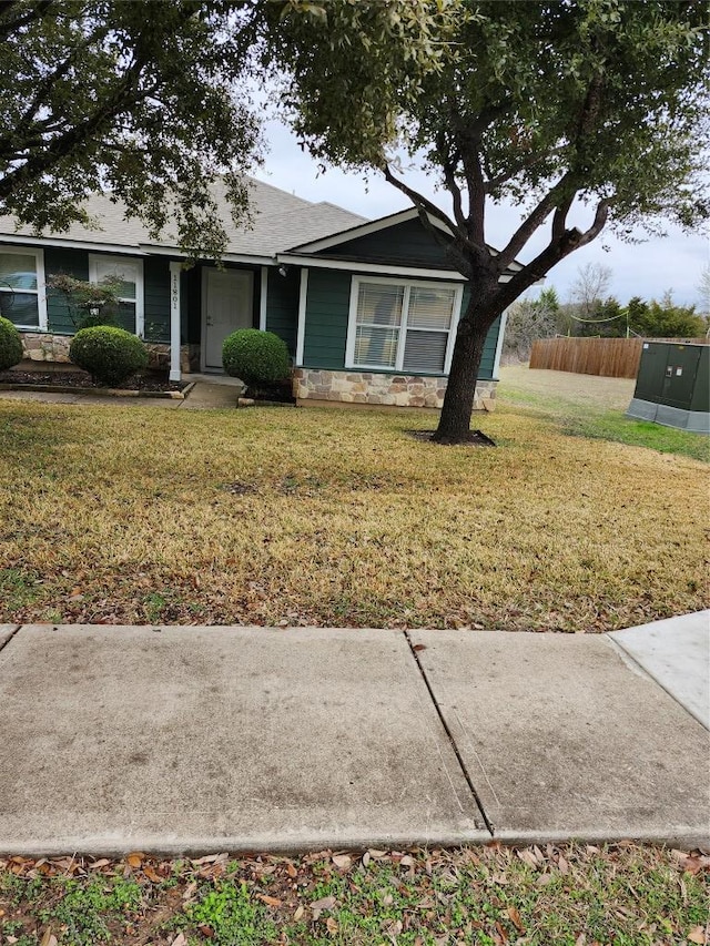 view of front of home featuring stone siding, fence, and a front lawn