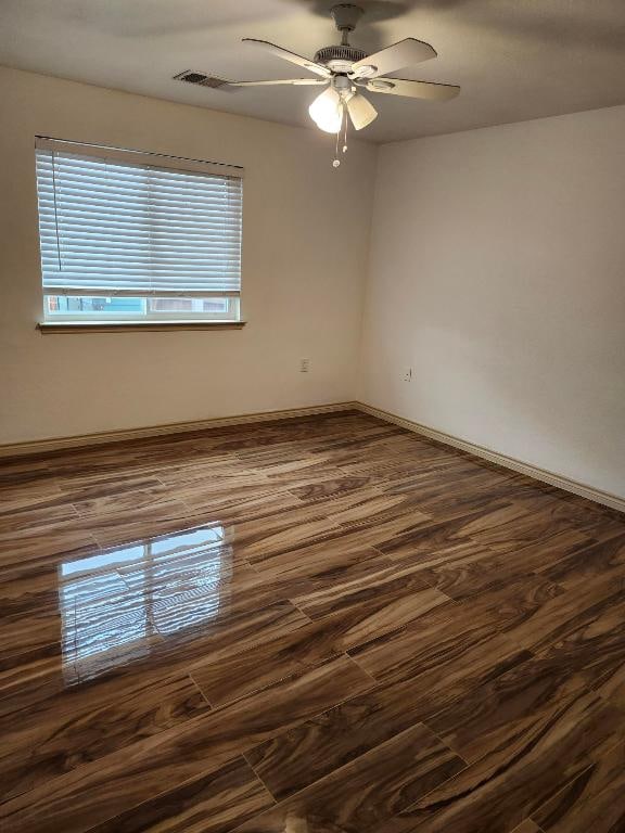 empty room with dark wood-style flooring, baseboards, a ceiling fan, and visible vents
