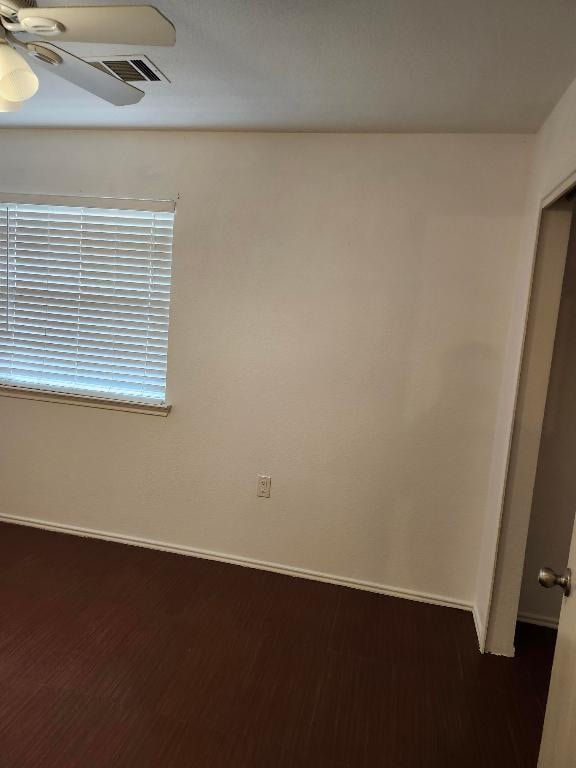 unfurnished room featuring baseboards, visible vents, dark wood-style flooring, and a ceiling fan