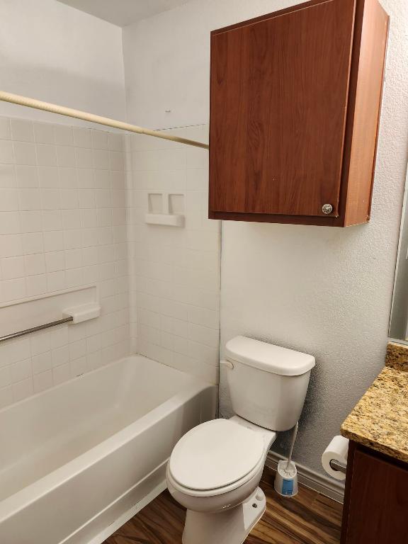 full bath with tub / shower combination, vanity, toilet, wood finished floors, and baseboards