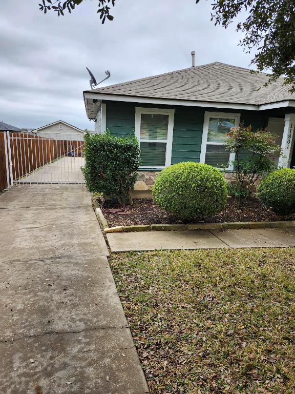 view of side of home with roof with shingles, driveway, and fence