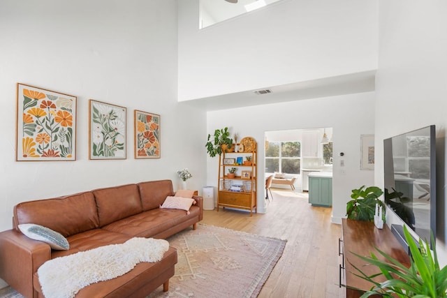 living room with visible vents, light wood-style floors, and a towering ceiling