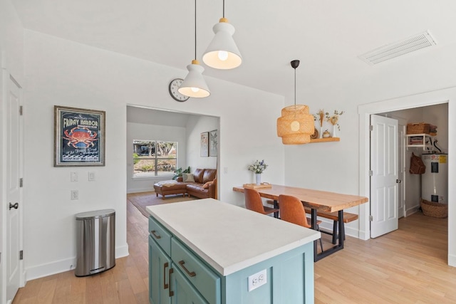 kitchen with visible vents, light wood finished floors, electric water heater, green cabinets, and light countertops