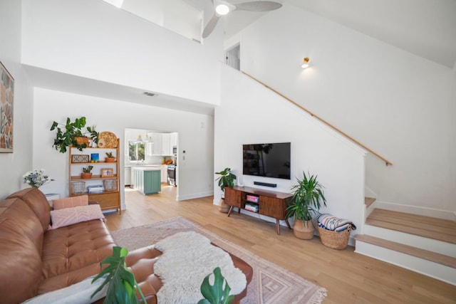 living room with stairway, baseboards, visible vents, high vaulted ceiling, and light wood-style flooring