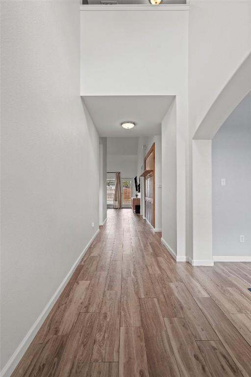 corridor with baseboards, arched walkways, and wood finished floors