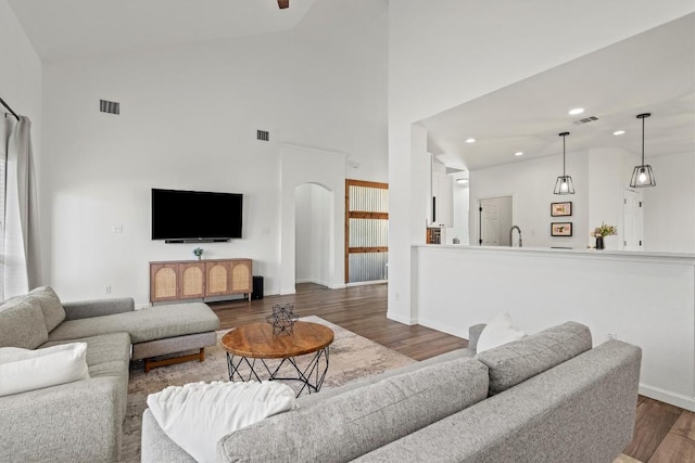 living area featuring high vaulted ceiling, wood finished floors, recessed lighting, arched walkways, and baseboards