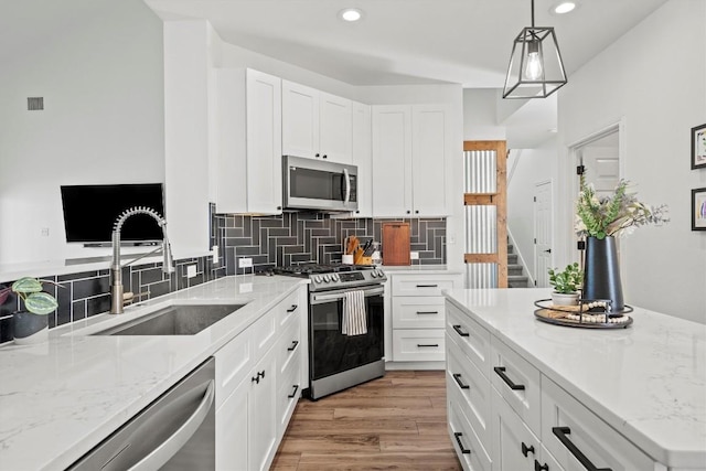 kitchen featuring light wood-type flooring, light stone counters, decorative backsplash, appliances with stainless steel finishes, and a sink