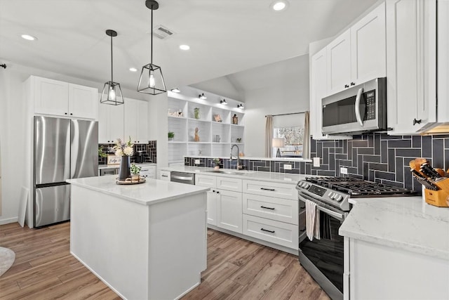 kitchen featuring light wood finished floors, a kitchen island, a peninsula, a sink, and appliances with stainless steel finishes