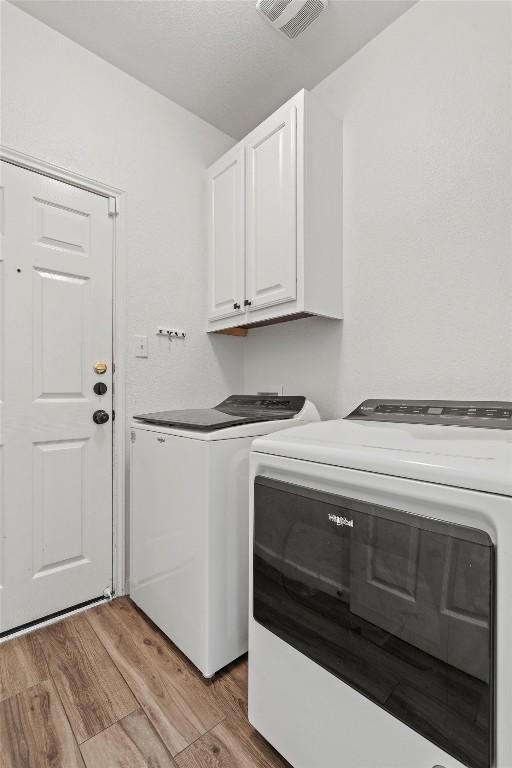 washroom featuring light wood-type flooring, visible vents, cabinet space, and independent washer and dryer