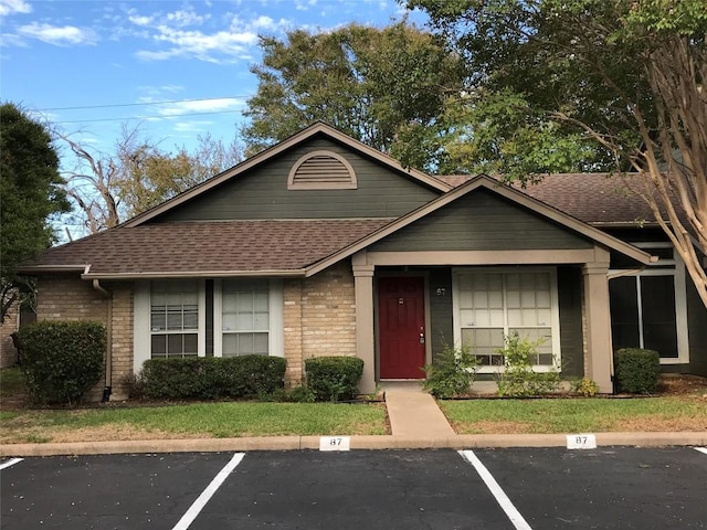 view of front of property featuring brick siding, roof with shingles, and uncovered parking