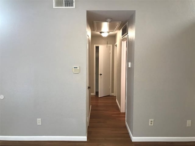 hallway with visible vents, baseboards, attic access, and wood finished floors