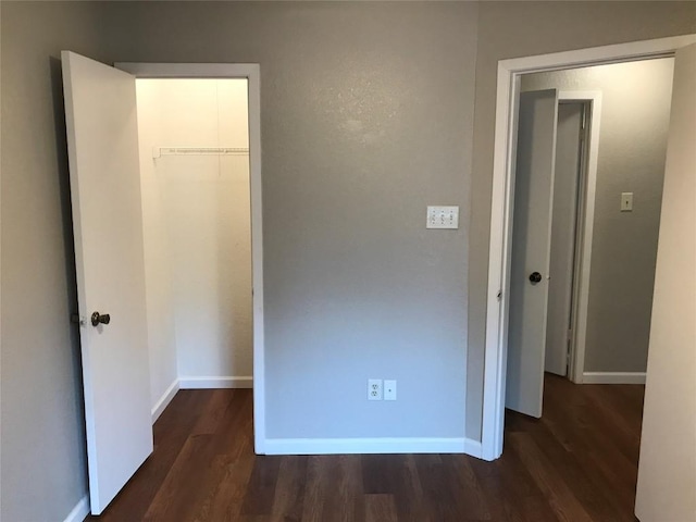 unfurnished bedroom with a spacious closet, a closet, baseboards, and wood finished floors