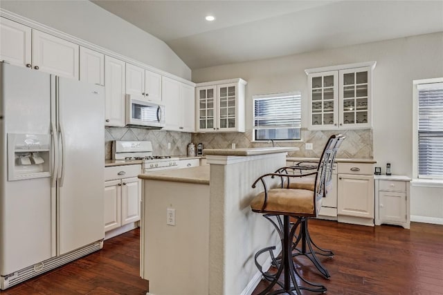 kitchen with dark wood-type flooring, a breakfast bar area, lofted ceiling, white cabinets, and white appliances