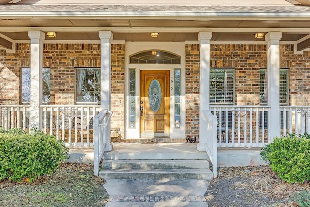 view of exterior entry featuring a porch, brick siding, and roof with shingles