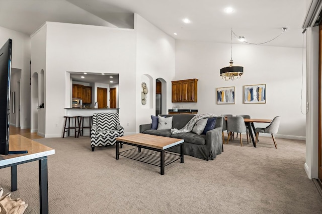 living room featuring baseboards, recessed lighting, arched walkways, a towering ceiling, and light carpet