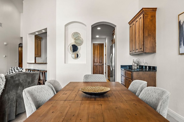 dining room with a high ceiling, recessed lighting, baseboards, and arched walkways