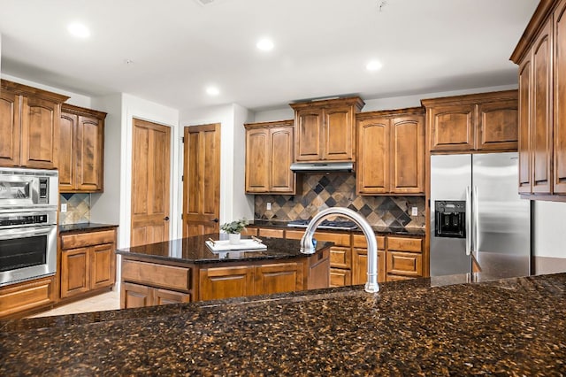 kitchen with dark stone countertops, recessed lighting, stainless steel appliances, under cabinet range hood, and backsplash