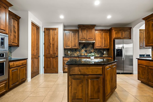 kitchen with tasteful backsplash, under cabinet range hood, light tile patterned floors, dark stone countertops, and stainless steel appliances