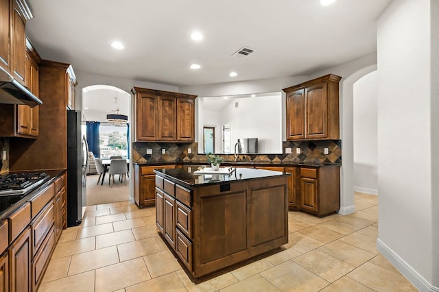 kitchen featuring a kitchen island, cooktop, decorative backsplash, freestanding refrigerator, and arched walkways