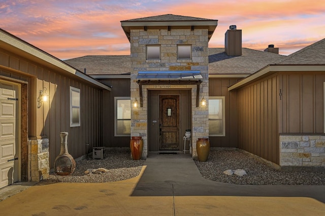 property entrance with roof with shingles, board and batten siding, stone siding, and a chimney