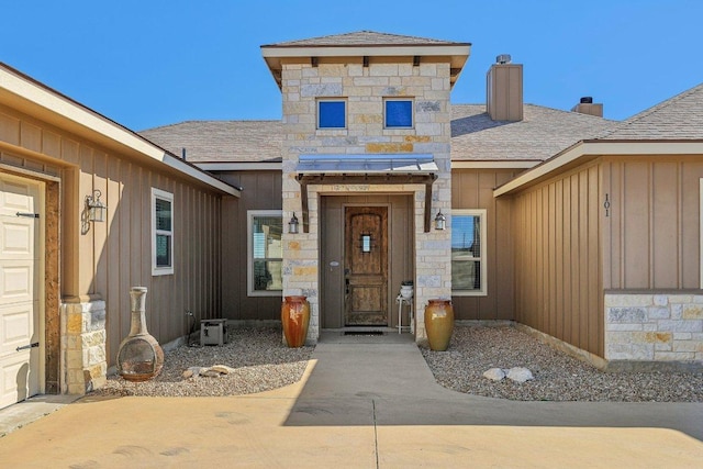 property entrance featuring stone siding, board and batten siding, a chimney, and roof with shingles