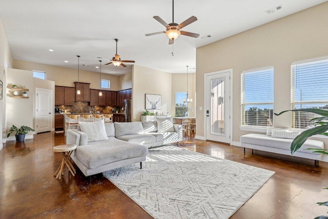 living area featuring visible vents, baseboards, ceiling fan, concrete flooring, and a high ceiling