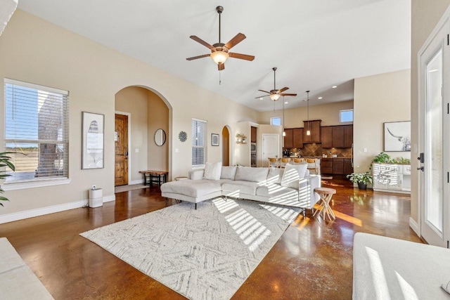 living room with arched walkways, plenty of natural light, concrete flooring, and ceiling fan