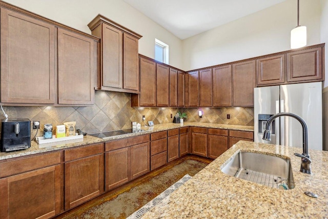 kitchen featuring light stone counters, a sink, stainless steel refrigerator with ice dispenser, black electric stovetop, and backsplash