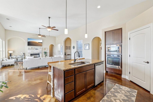 kitchen with light stone counters, arched walkways, a sink, stainless steel appliances, and concrete flooring