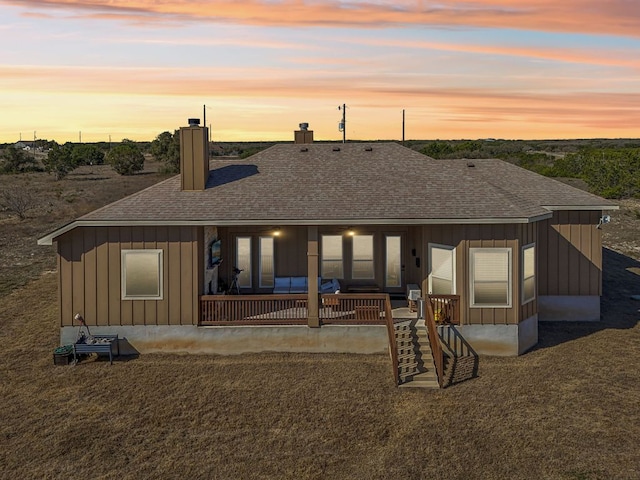 back of property at dusk featuring board and batten siding, a chimney, and roof with shingles